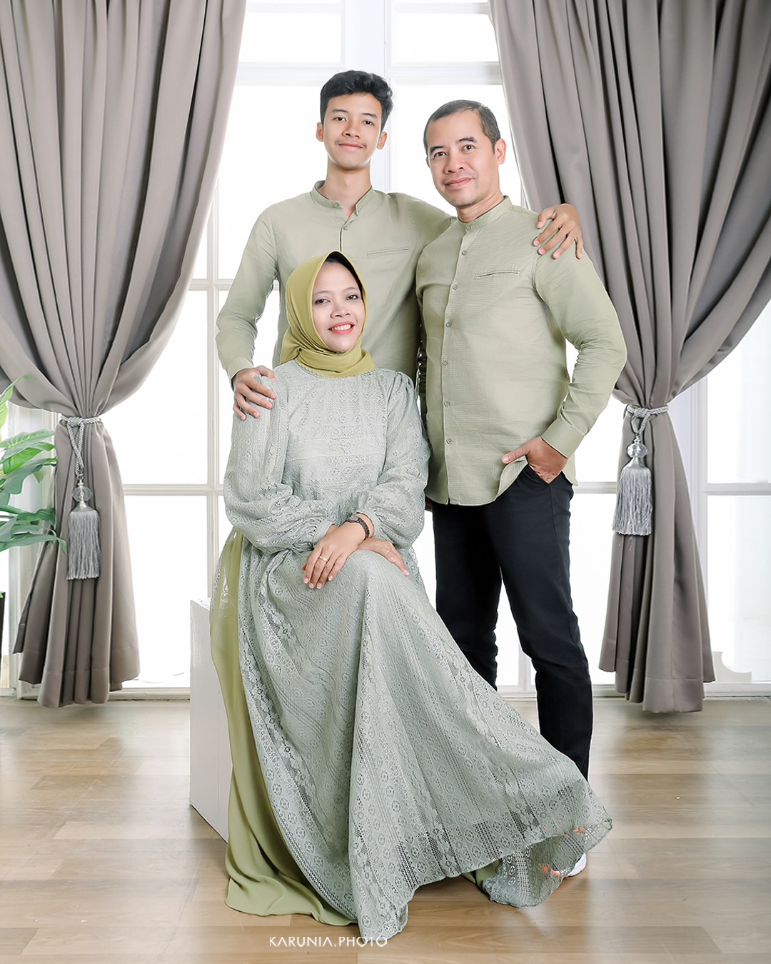 Three siblings sitting on wooden steps in coordinating outfits with genuine smiles and relaxed poses